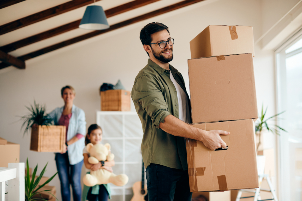 Happy father carrying stack of cardboard boxes while relocating in a new apartment